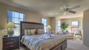 A bedroom with a large bed, two bedside tables, a ceiling fan, and a view of the outside through large windows. - Villa w/ Game Room: 10 Mi to Disney! (Davenport)