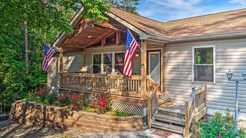 A cabin with a wooden porch, two American flags, and a landscaped garden with red flowers.