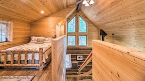 Un dormitorio de cabaña de madera con cama, ventana, ventilador de techo y una escalera.