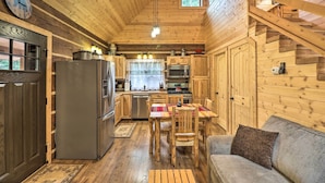 Interior de una cabaña de madera con cocina, comedor y una escalera.