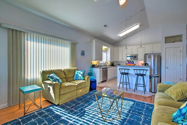 A modern kitchen with white cabinets, a microwave, and a refrigerator. There is a dining area with a bar stool and a small table.