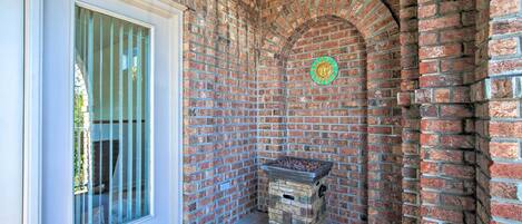 A corner of a building with a brick wall, a window with metal bars, and a stone fireplace.