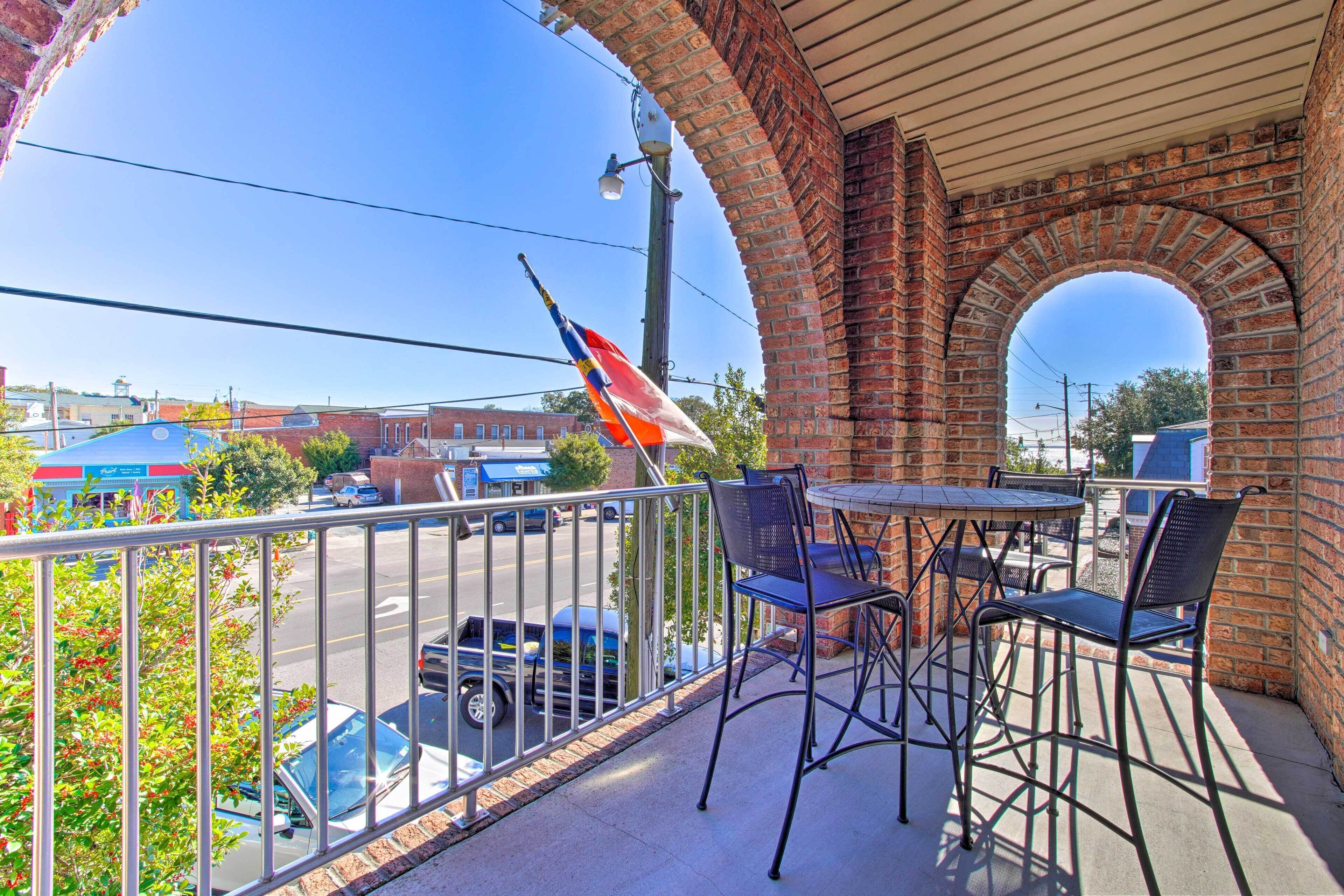 A balcony with a brick arch, metal railing, and a table with chairs.