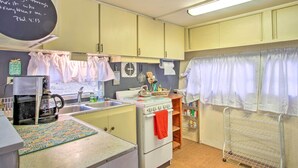 A kitchen with a stove, sink, and coffee maker. There is a chalkboard with a Bible verse, and a window with curtains. - Athens Vintage Fishing Cabin on Elk River! (Athens)