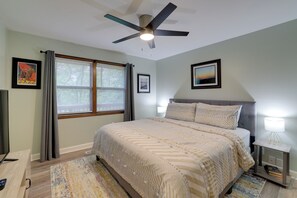 A bedroom with a bed, a ceiling fan, a window with curtains, and framed pictures on the wall.