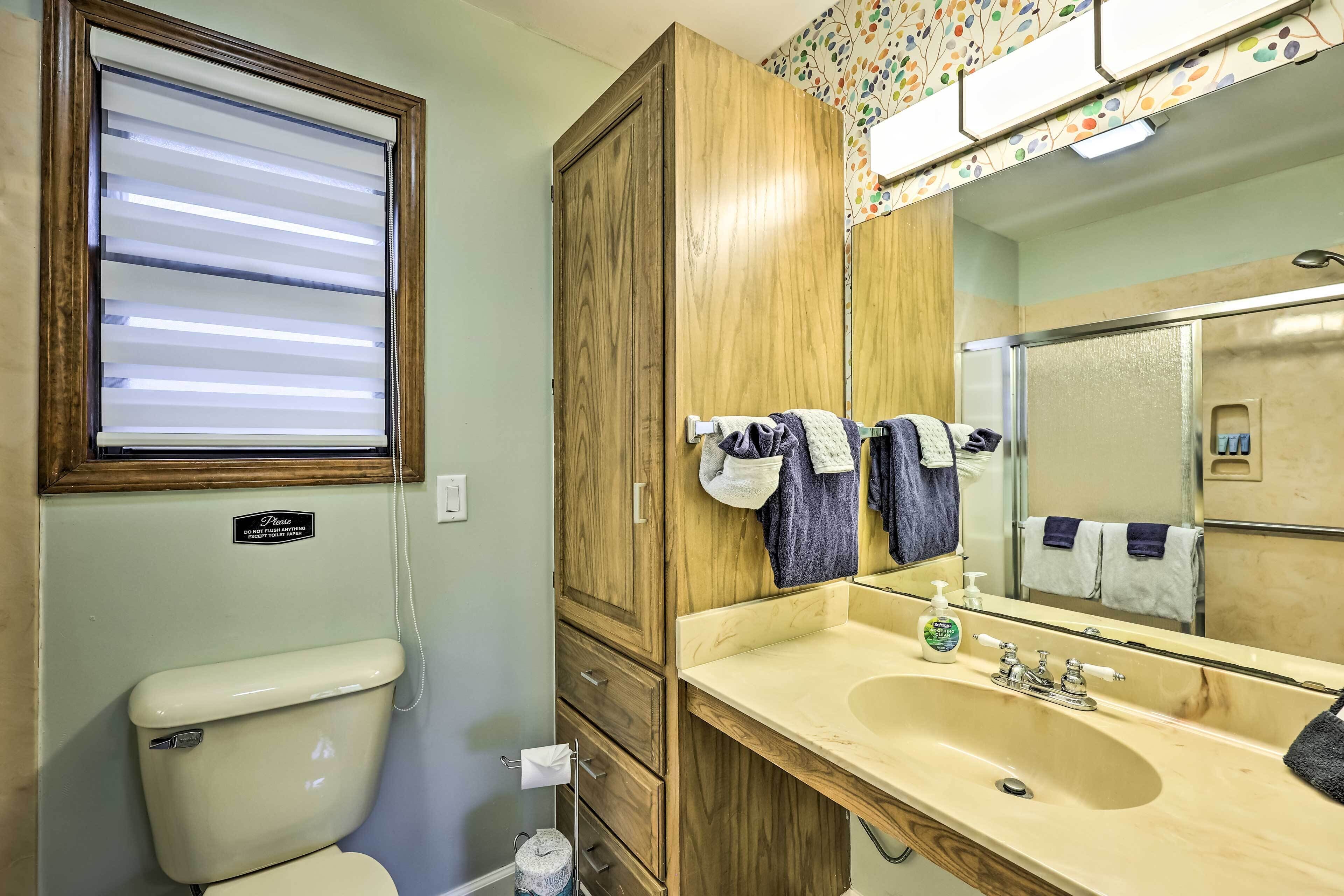 A bathroom with a toilet, a sink, a mirror, and a window with blinds.