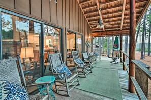 A covered outdoor seating area with rocking chairs and tables, large windows, and a wooden ceiling.