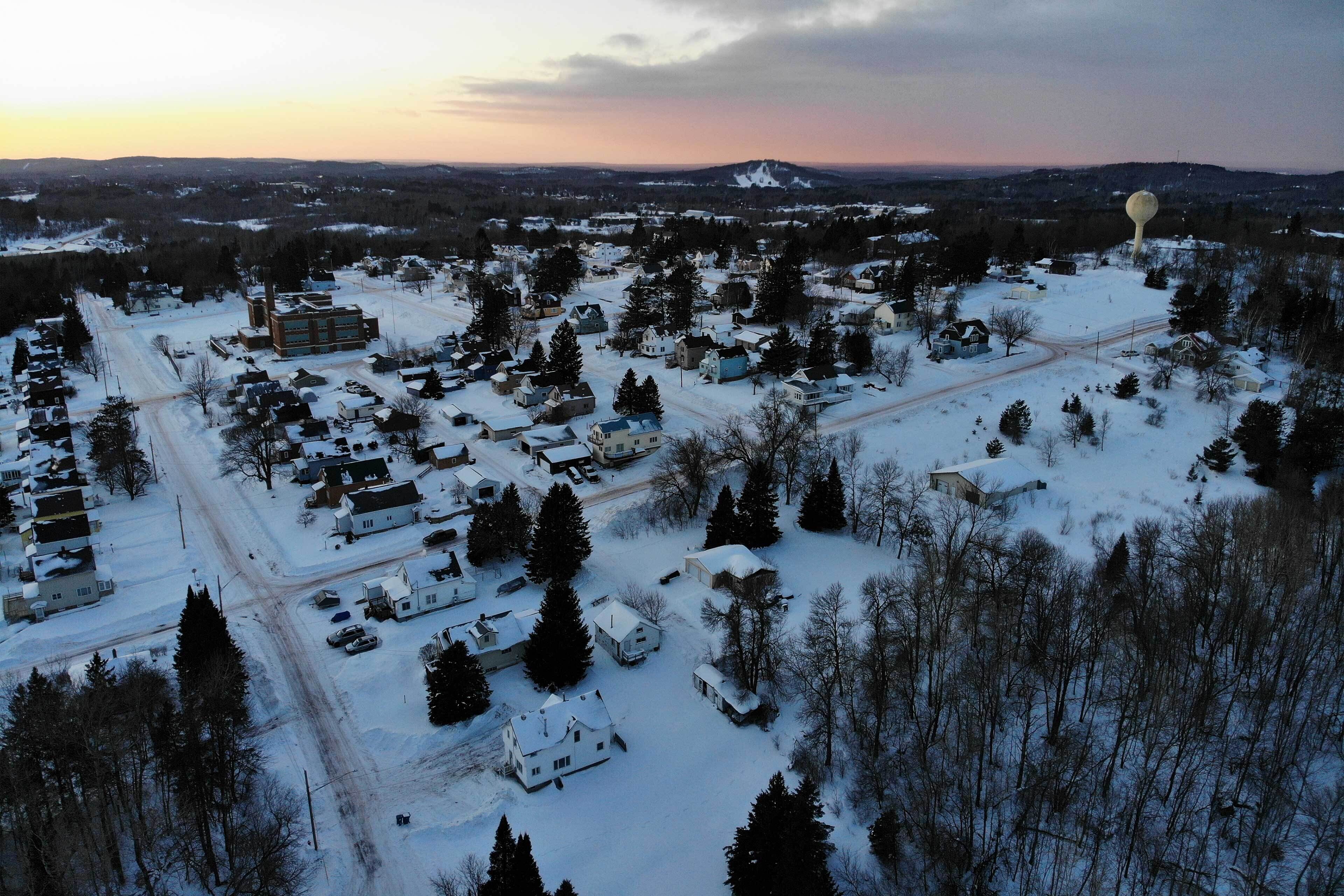 A snow-covered residential area with houses, roads, and a large building in the center.