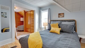 A bedroom with a large bed, a wooden wardrobe, a mirror, and a window with curtains.