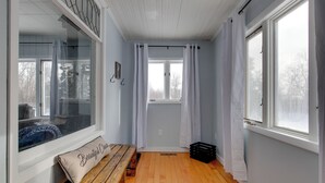A room with a wooden bench, a bench cushion, a window with curtains, and a door leading outside.