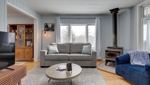 A living room with a grey sofa, a coffee table, a TV, a bookshelf, and a wood-burning stove.