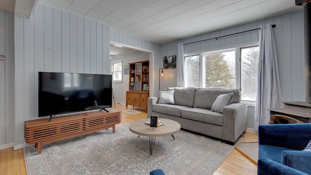 A modern living room with a flat-screen TV, a grey sofa, a blue armchair, and a wooden entertainment unit.