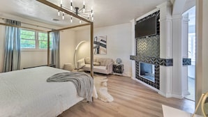 Ein Schlafzimmer mit einem großen Bett, einer modernen Kronleuchter, einem Kamin und Blick ins Freie.