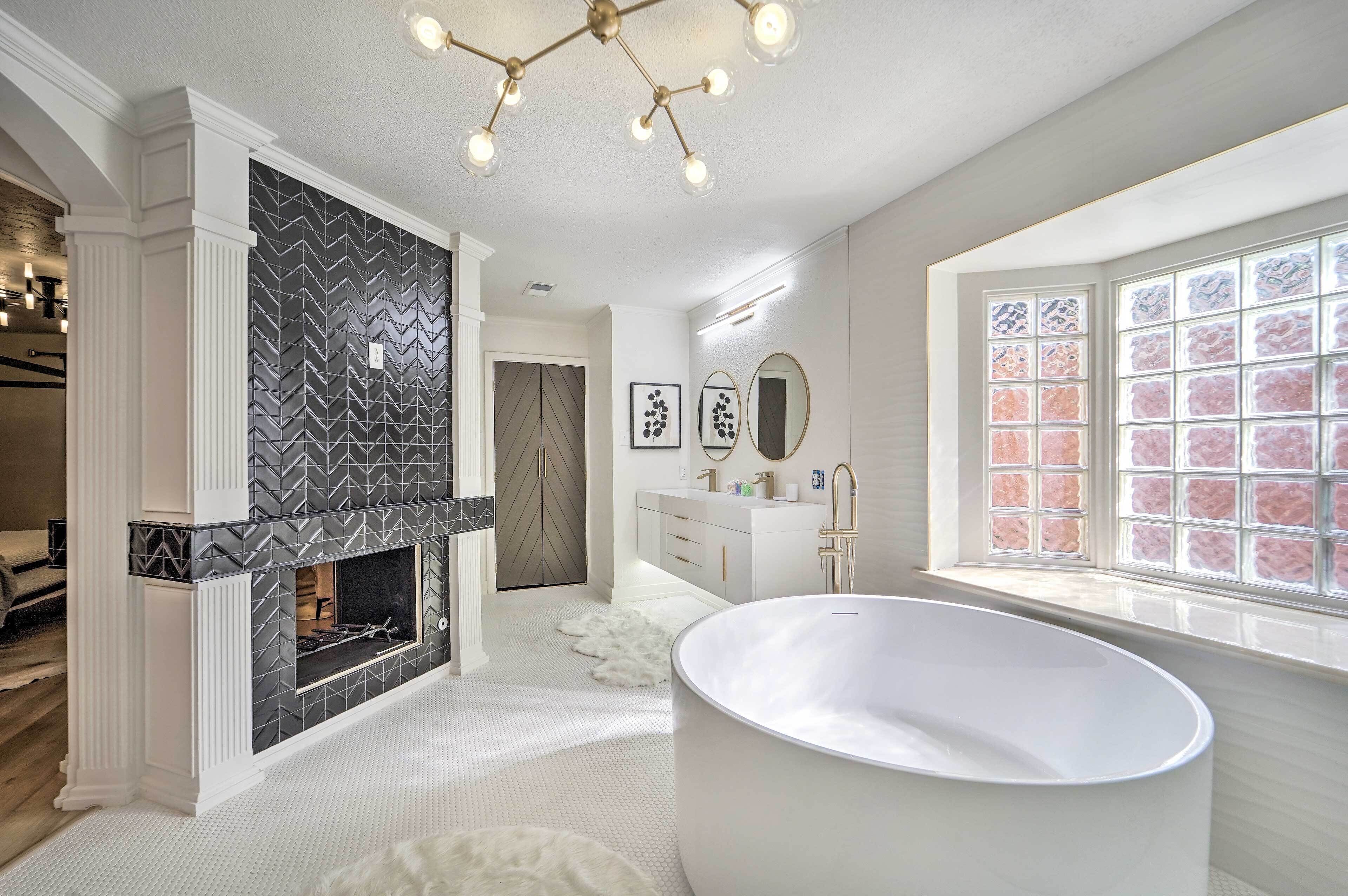 A modern bathroom with a freestanding bathtub, a fireplace, and a large window with pink-tinted glass.