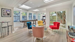 Ein geräumiges Wohnzimmer mit großem Fenster, einem Klavier und bunten Sesseln.