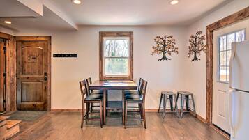 A dining area with a wooden table and chairs, a window with a view, and a refrigerator.