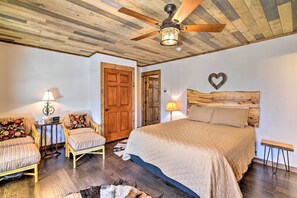 Un dormitorio con una cama grande, dos sillones tapizados, un ventilador de techo de madera y un cabecero de madera.