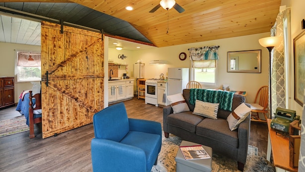 A spacious living area with a large wooden door, a ceiling fan, and a cozy seating area with a blue armchair and a gray sofa.
