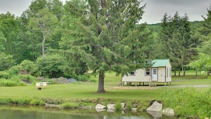 A small cabin with a green roof, surrounded by lush greenery and a pond.