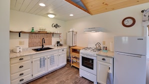 A kitchen with white cabinets, a wooden ceiling, a sink, a stove, and a refrigerator.