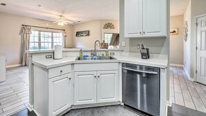 A modern kitchen with white cabinetry, a stainless steel dishwasher, and a ceiling fan. - Cozy Wilmington Bungalow ~ 6 Mi to Beaches! (Wilmington)