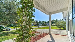A covered porch with a concrete floor, a tree with green leaves, and a clear view of a street and houses in the background. - Cozy Wilmington Bungalow ~ 6 Mi to Beaches! (Wilmington)