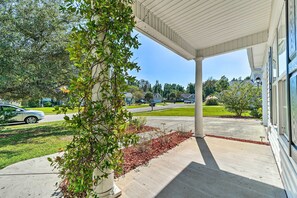 A covered porch with a concrete floor, a tree with green leaves, and a clear view of a street and houses in the background. - Cozy Wilmington Bungalow ~ 6 Mi to Beaches! (Wilmington)