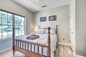 A bedroom with a wooden bed, a large window, and two wall-mounted pictures. - Cozy Wilmington Bungalow ~ 6 Mi to Beaches! (Wilmington)