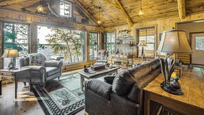 A cozy cabin interior with a wooden ceiling, large windows, a leather sofa, a desk, and a lamp. - Quiet Lakefront Conover Cabin Near ATV Trails (Conover)