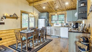 A rustic kitchen with wooden beams, a chandelier, and a 'Welcome' bear decoration. - Quiet Lakefront Conover Cabin Near ATV Trails (Conover)