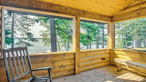 A wooden cabin with a bench and a chair by a large window overlooking a lake and trees. - Quiet Lakefront Conover Cabin Near ATV Trails (Conover)