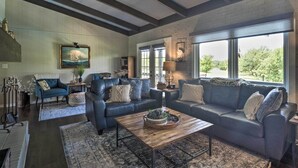 A spacious living room with a large window, a blue sofa set, a wooden coffee table, and a framed picture on the wall. - Chic Family-friendly Home With Outdoor Oasis! (Lampasas)