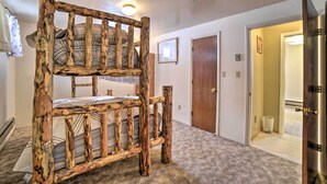 Un letto a castello con una struttura in legno rustica in un corridoio con pavimento rivestito di moquette, una porta e un lampadario al soffitto.