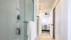 A modern bathroom with a glass shower enclosure, a white towel hanging on the door, and toiletries on a shelf. - Modern Kanab Cottage w/ View < 1 Mi to Hiking! (Kanab)