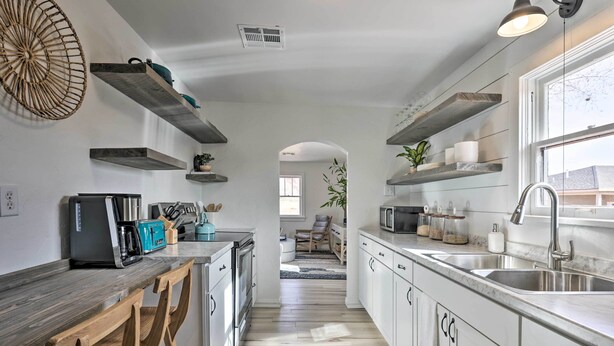 A modern kitchen with white cabinets, a wooden countertop, and built-in appliances. There are shelves above the counter and a view into the dining area. - Modern Kanab Cottage w/ View < 1 Mi to Hiking! (Kanab)