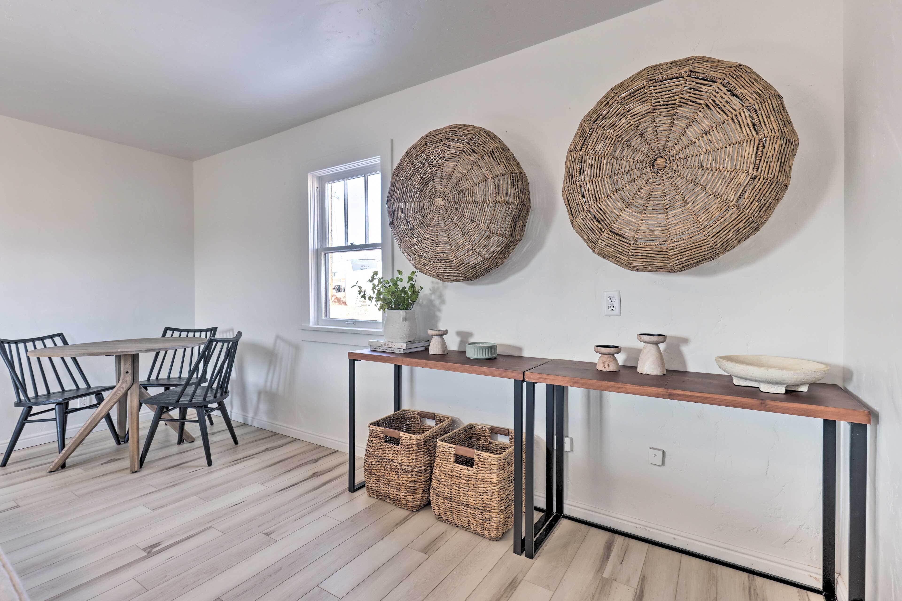 A dining area with a wooden table and chairs, a woven wall hanging, and wicker baskets under the table.