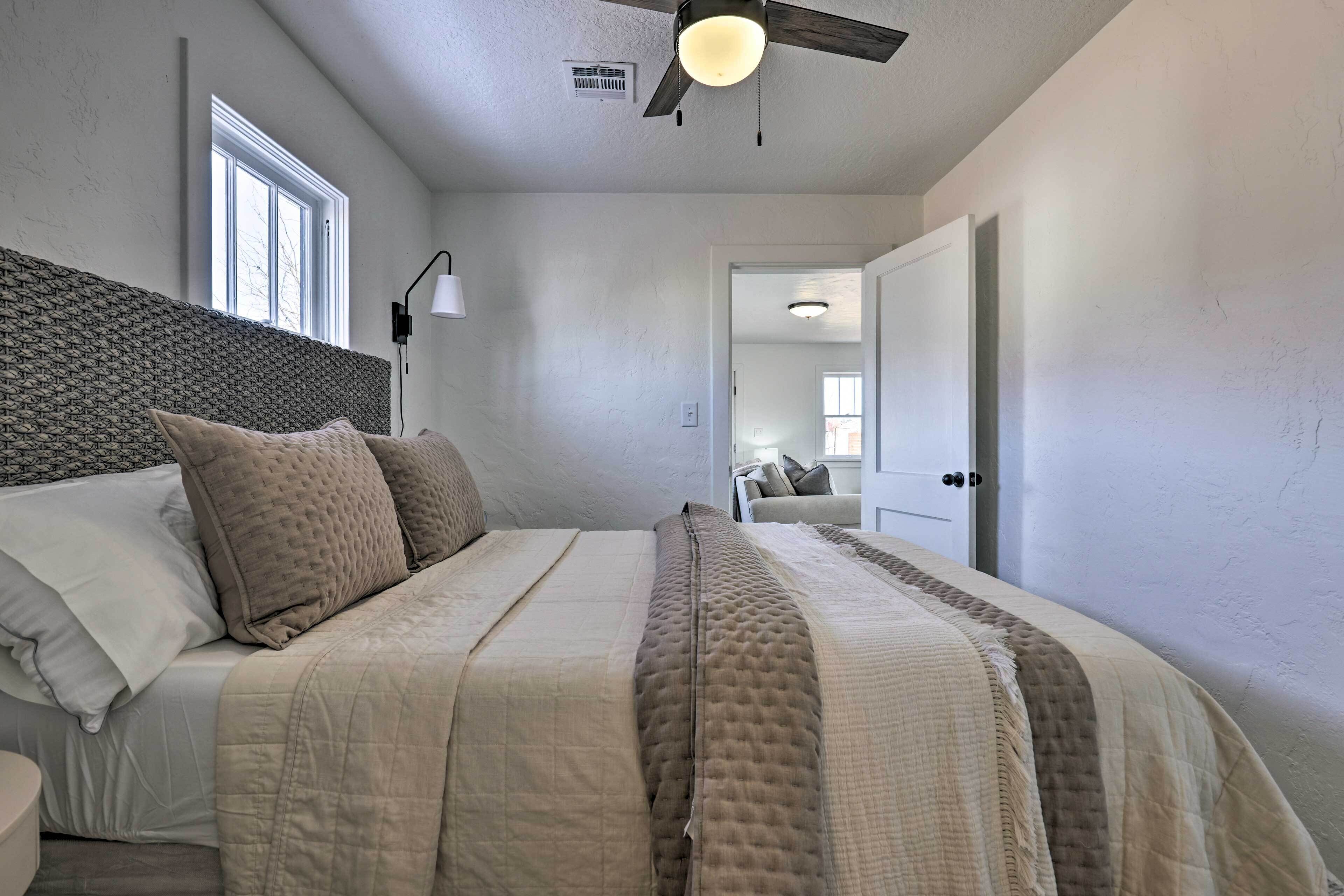 Un dormitorio con cama, ventilador de techo, ventana y puerta que da a otra habitación.