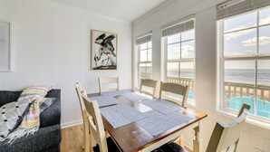 Ruokailutilassa on puinen pöytä ja tuolit, suurista ikkunoista avautuu näkymä merelle ja seinällä on taulu.