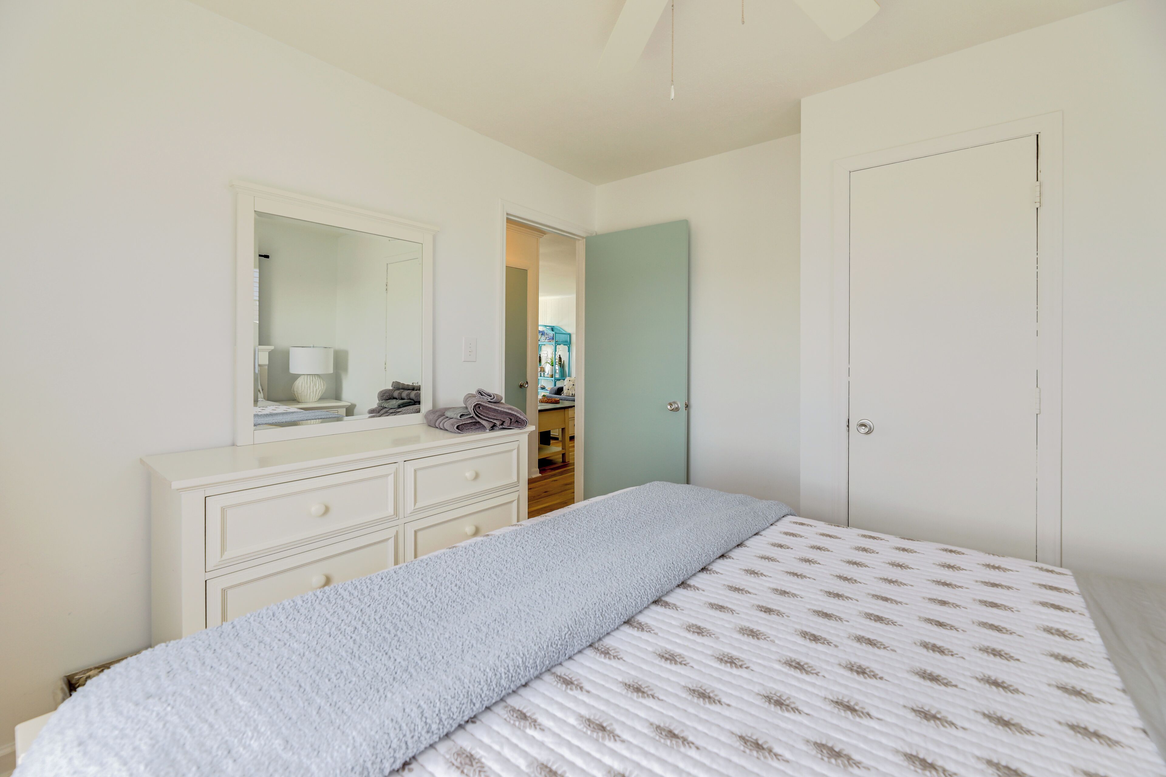 Une chambre à coucher avec un lit, une commode, un miroir et une porte.