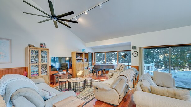 A spacious living room with a ceiling fan, a piano, and a large window with a snowy view. - Ultimate Mountain Home w/ Hot Tub! (Tannersville)