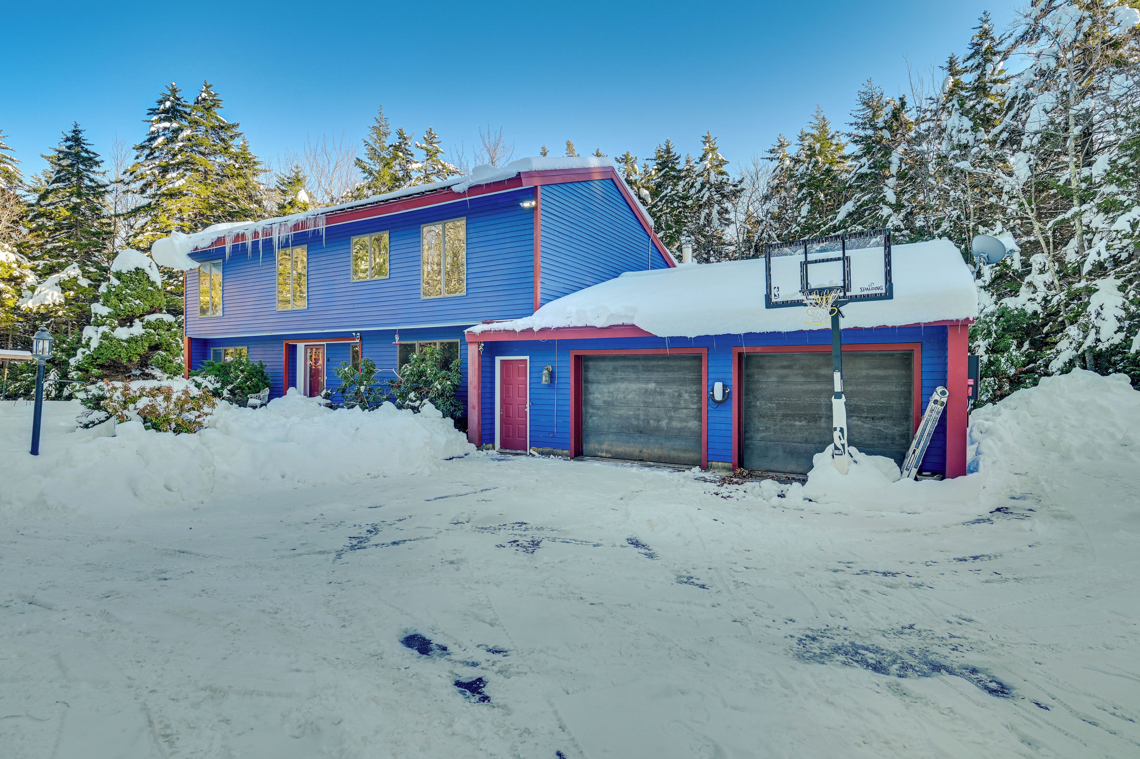A blue house with two garage doors, surrounded by snow and trees.