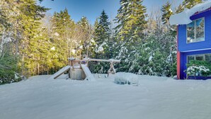 A snowy outdoor area with a wooden play structure and a blue building. - Ultimate Mountain Home w/ Hot Tub! (Tannersville)