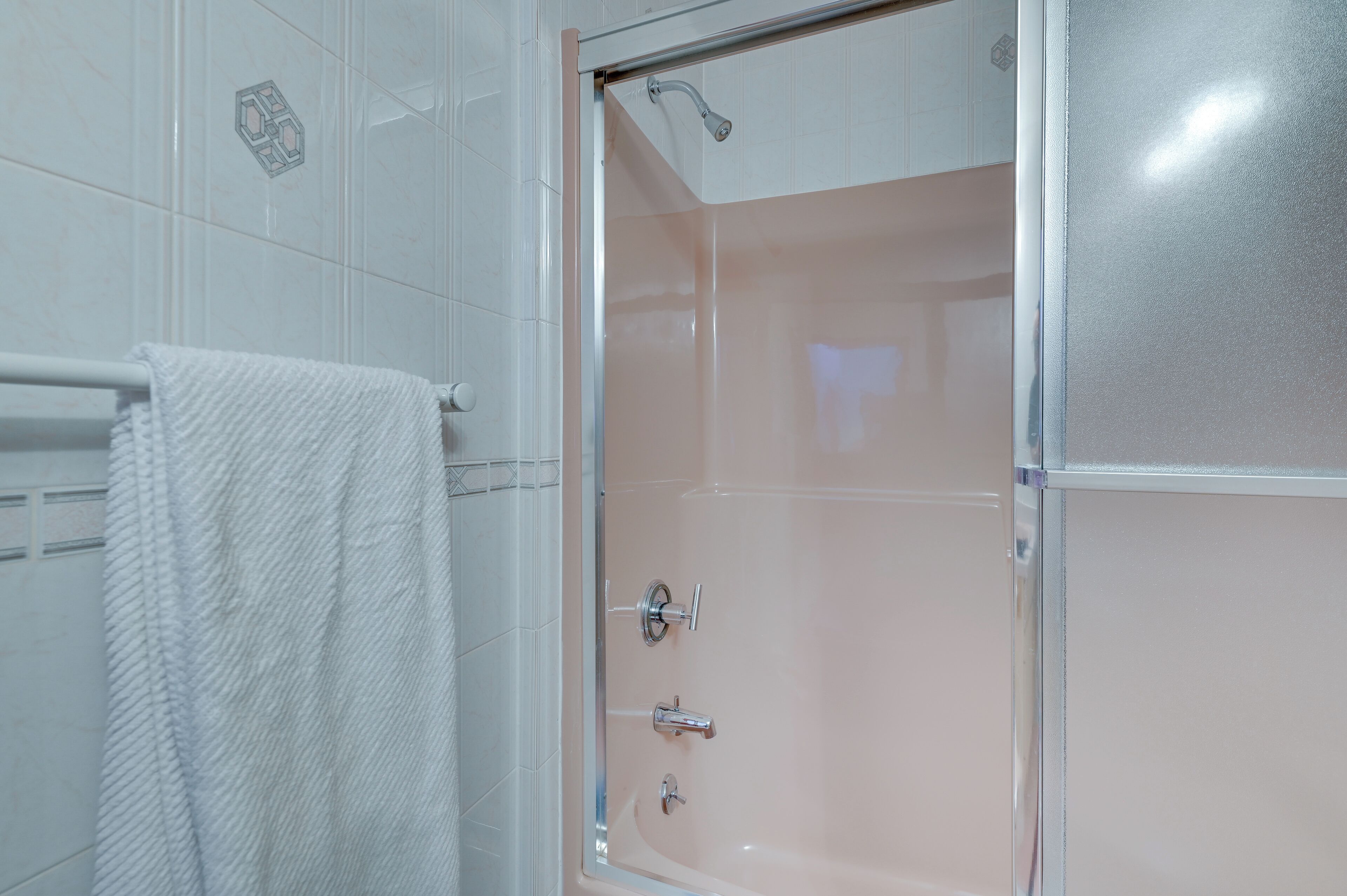 A shower with a glass door, a towel rack with a towel, and a hexagonal tile pattern on the wall.