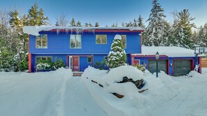 A blue house with a red door and garage doors, surrounded by snow-covered trees and a snow-covered driveway. - Ultimate Mountain Home w/ Hot Tub! (Tannersville)