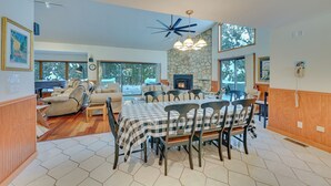 A spacious living room with a fireplace, a dining area with a checkered tablecloth, and a large window overlooking a snowy landscape. - Ultimate Mountain Home w/ Hot Tub! (Tannersville)