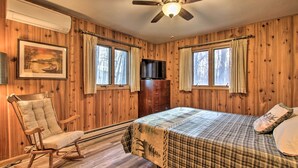 Una habitación con paneles de madera, una cama, un sillón mecedor y un ventilador de techo.