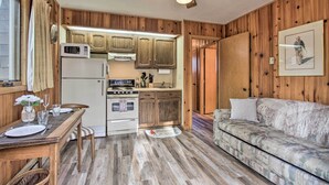 Cocina compacta con armarios de madera, microondas y estufa. Hay una mesa de comedor con sillas y un sofá en la sala.