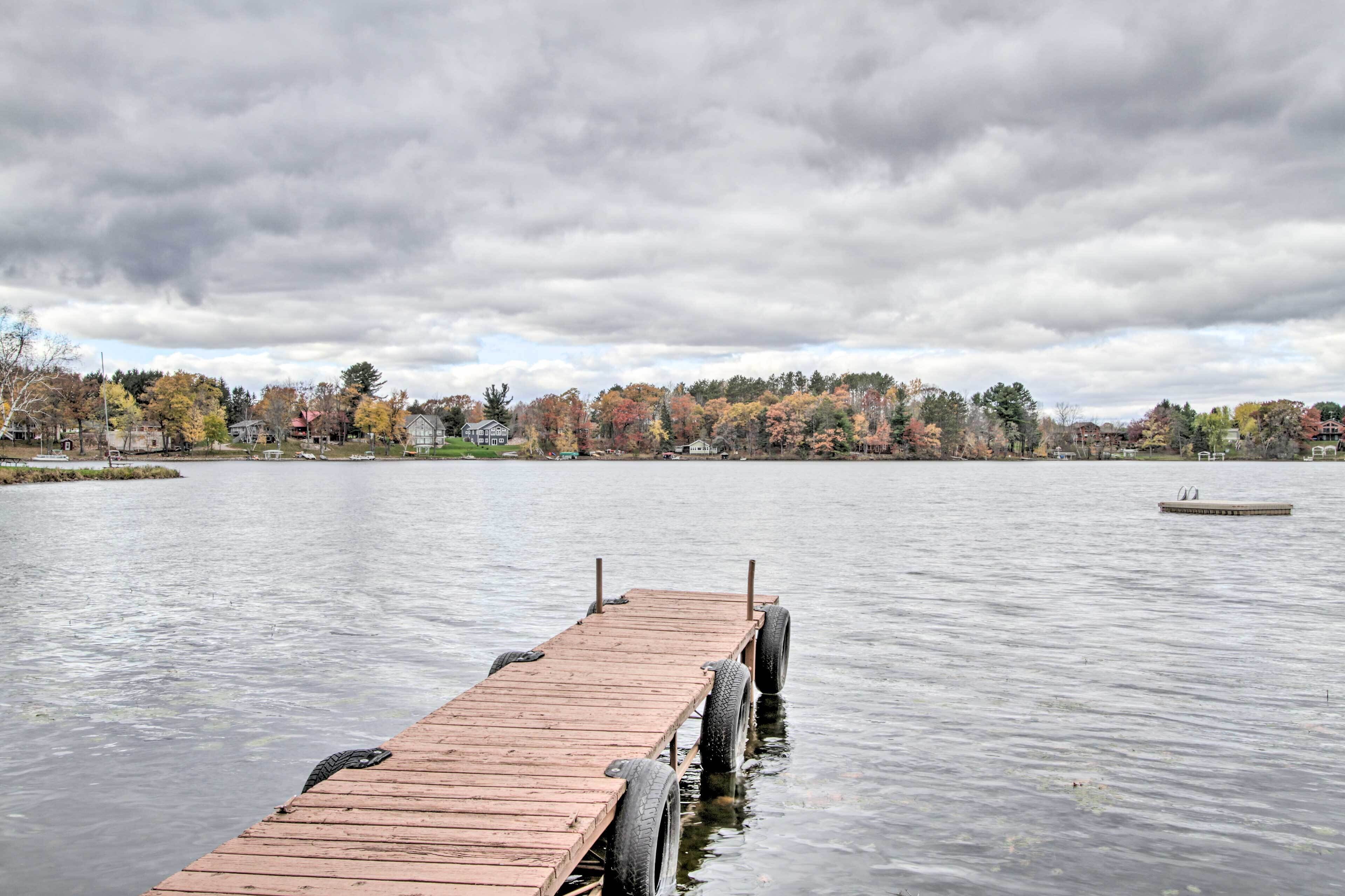 A wooden dock extending into a calm lake with a backdrop of autumn-colored trees and houses.