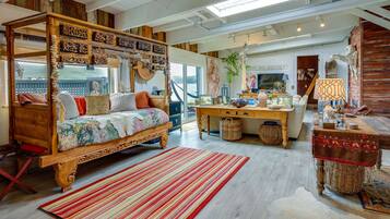 A cozy, rustic bedroom with a four-poster bed, a wooden desk, and a view of the outdoors.