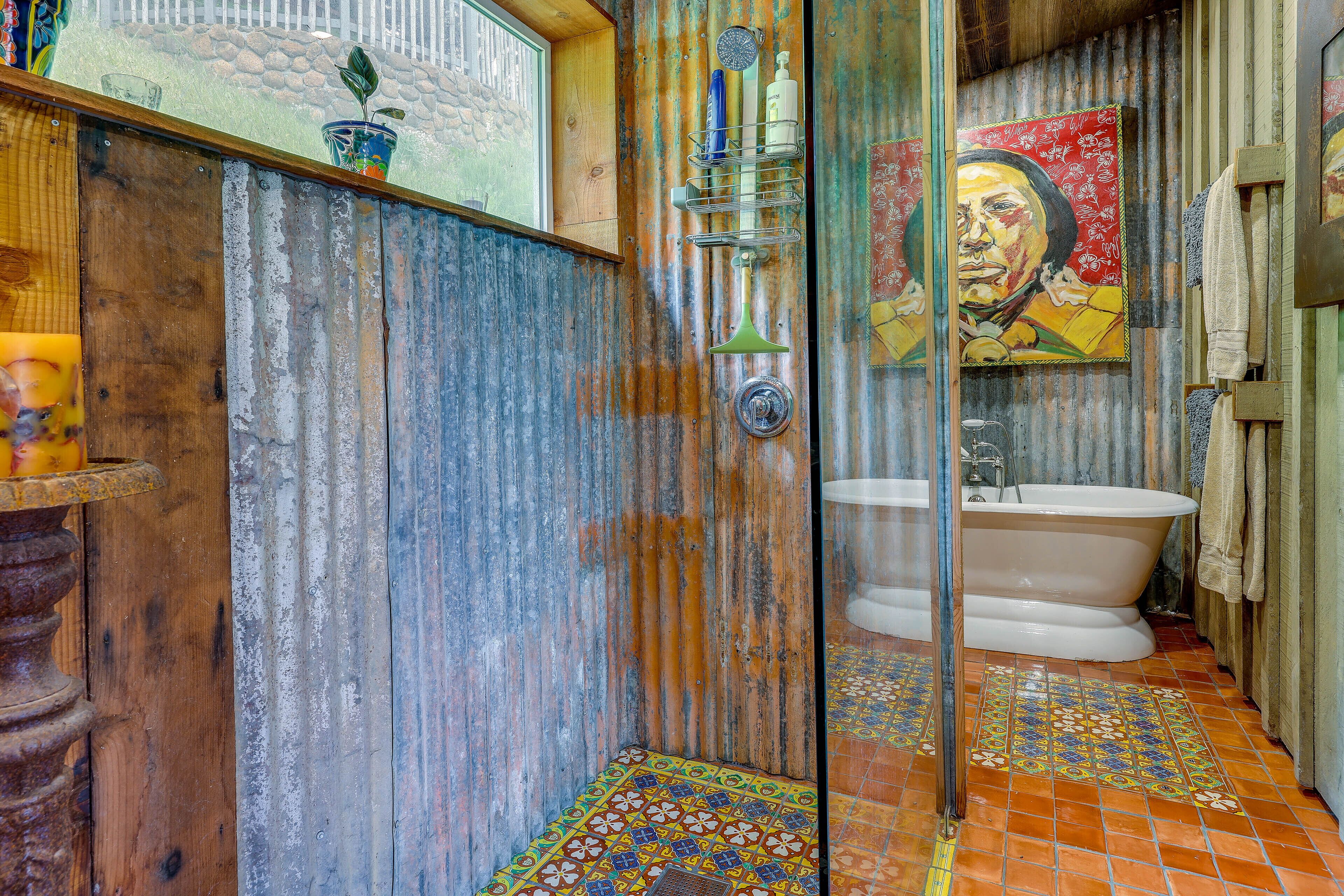 A rustic bathroom with a wooden shower enclosure, a vintage bathtub, and a colorful tiled floor.